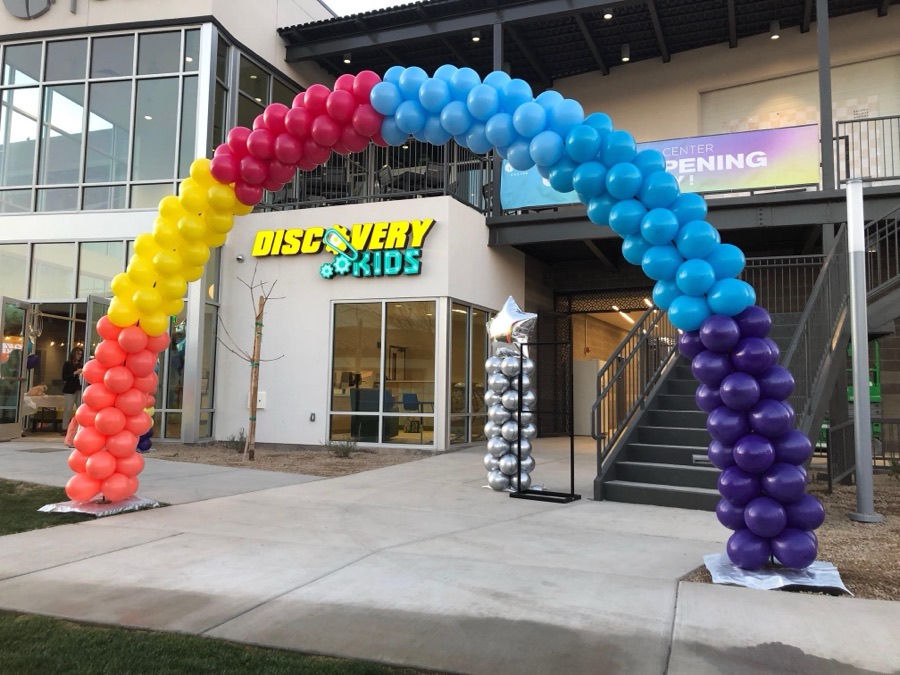 Rainbow balloon arch spanning a storefront entrance for a grand opening by AZ Party Mart