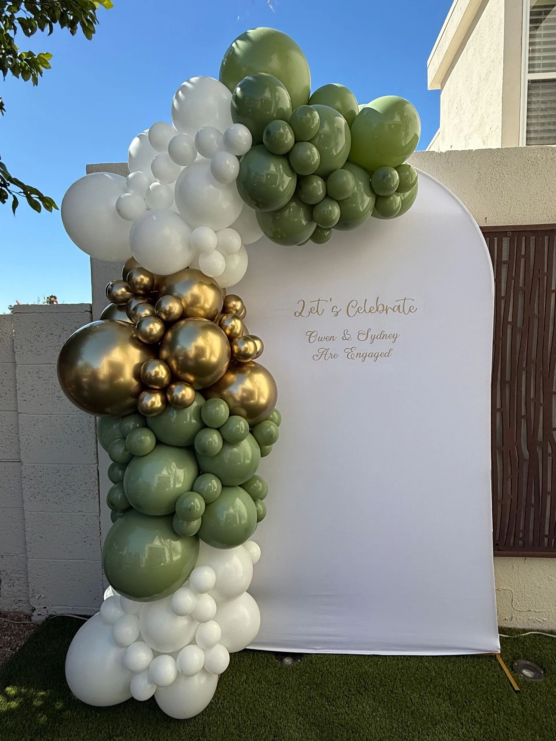 Green, white and gold organic balloon garland on an outdoor backdrop by AZ Party Mart
