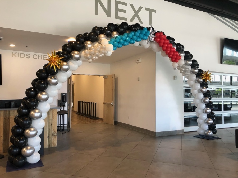 Black, white, teal and red balloon arch over an interior doorway by AZ Party Mart