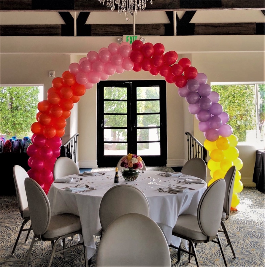 Rainbow balloon arch framing French doors above a banquet table