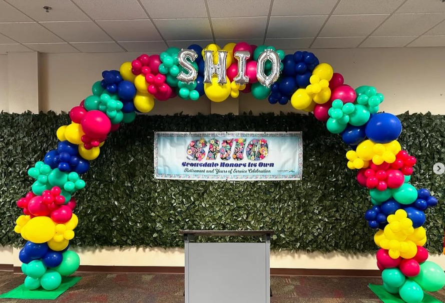 Primary-colour balloon arch over a green hedge wall by AZ Party Mart