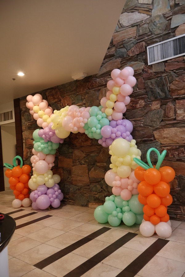 Pastel organic balloon letter with carrot accents on a stone wall by AZ Party Mart