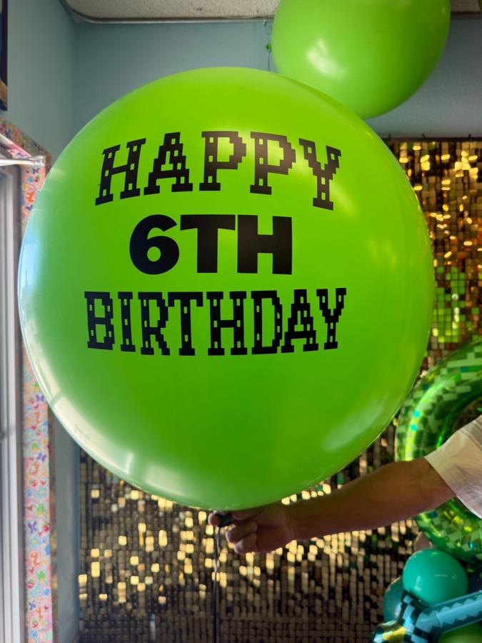 Giant green birthday balloon against a gold sequin backdrop by AZ Party Mart