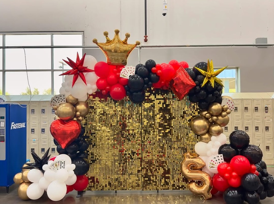 Casino-themed red, black and gold balloon garland framing a gold sequin backdrop