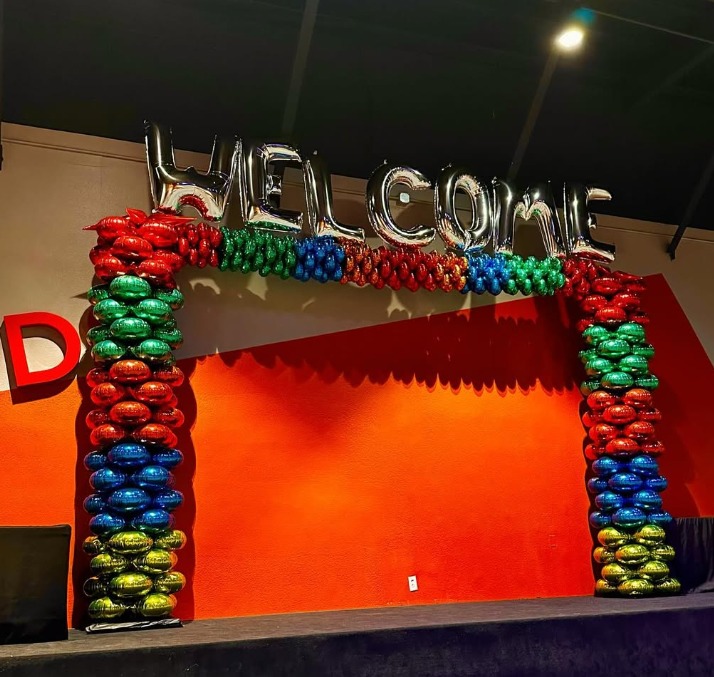 Rainbow balloon arch framing a stage with a welcome banner