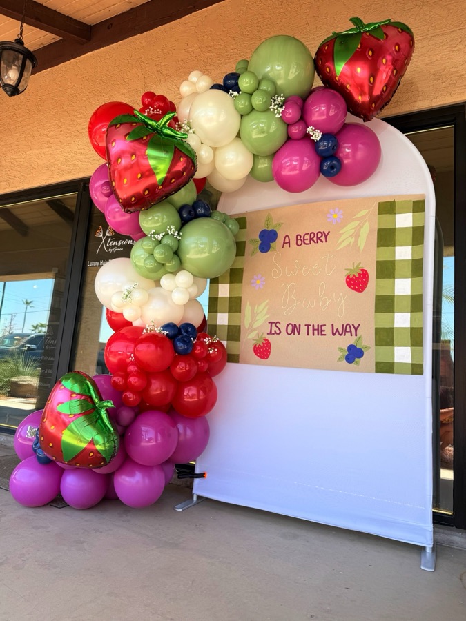 Berry-themed balloon garland framing a sign reading A Berry Sweet Baby Is On The Way