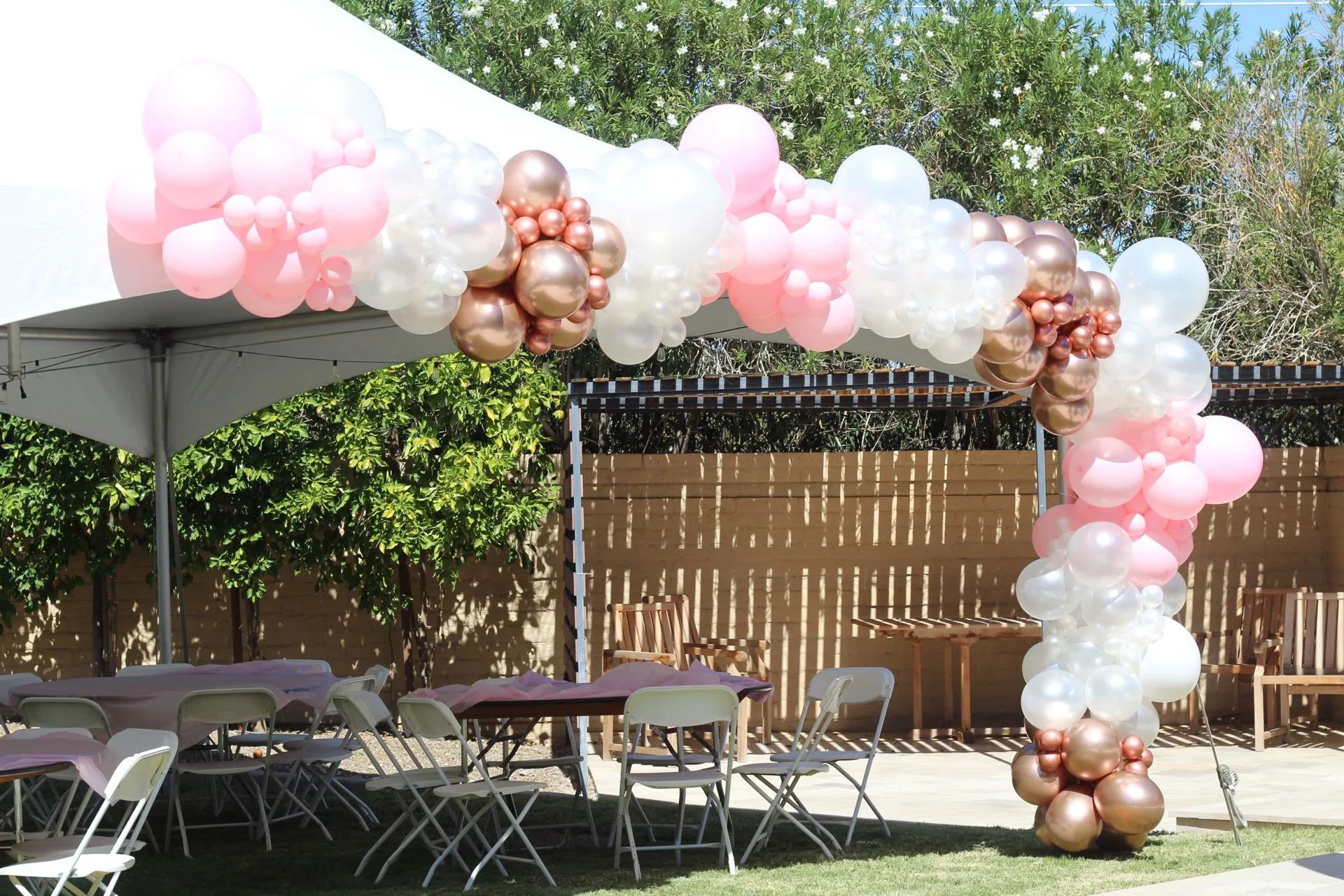 Pink, white, and gold balloon arch over beautifully set outdoor reception tables by AZ Party Mart